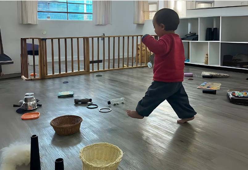 Criança caminha descalça em um ambiente preparado com cestos, objetos e materiais do cotidiano, explorando com liberdade — prática inspirada na abordagem Pikleriana, que valoriza o movimento espontâneo e o aprendizado pela descoberta.