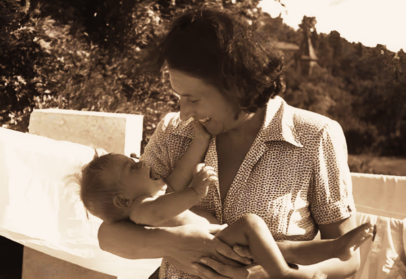 Emmi Pikler segura um bebê em seus braços, trocando olhares e sorrisos que expressam afeto e respeito — princípios fundamentais de sua abordagem sobre o cuidado e o desenvolvimento autônomo na primeira infância.