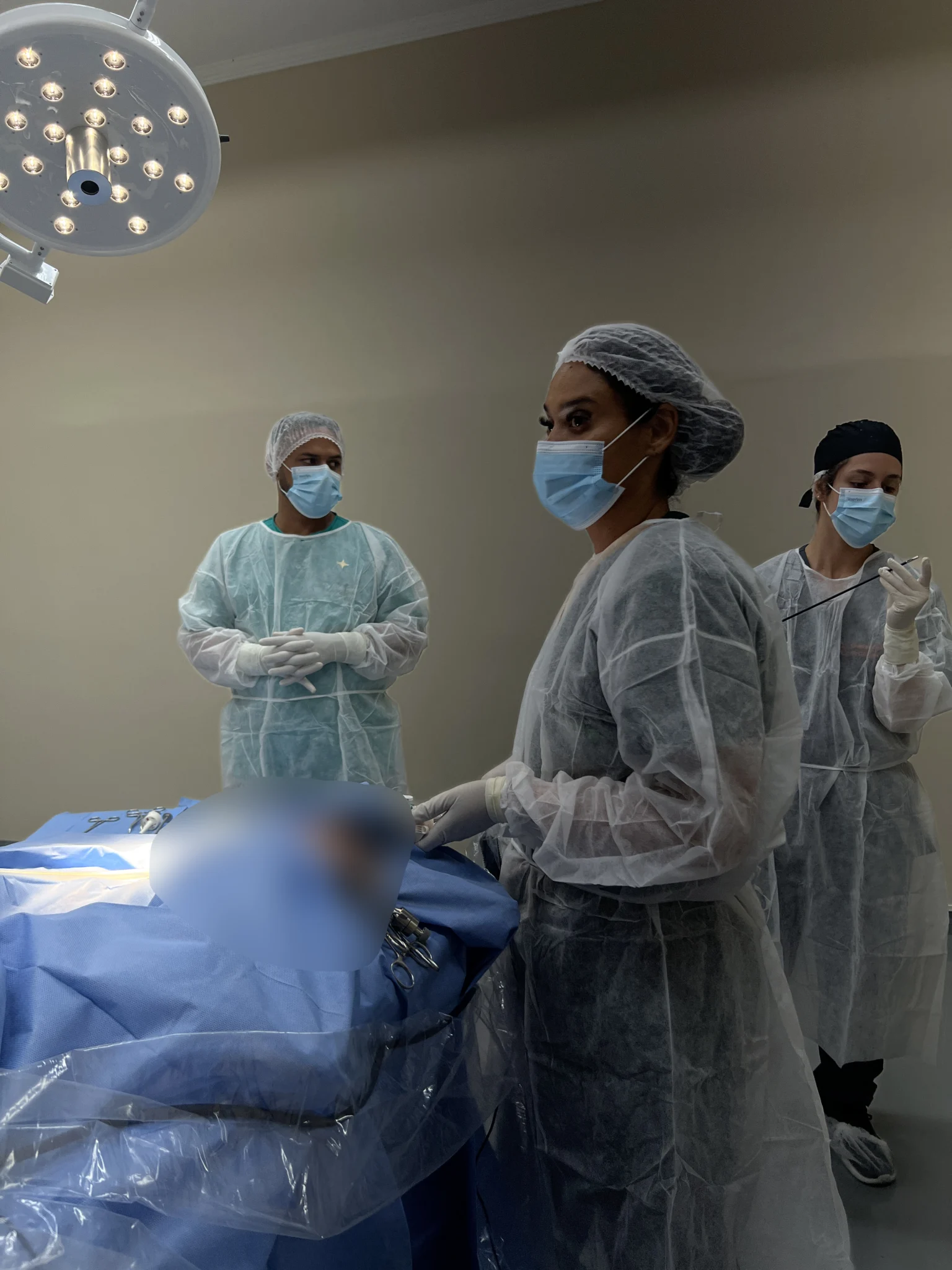 Equipe paramentada ao lado da mesa no centro cirúrgico, sob o foco de luz
