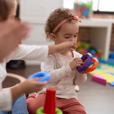 Criança manipulando brinquedos durante atividade psicomotora com acompanhamento de adulto