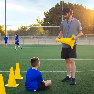 Treinador orientando criança durante atividade com cones em treino de futebol
