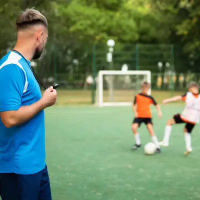 Treinador observando jovens atletas durante atividade de futebol em campo